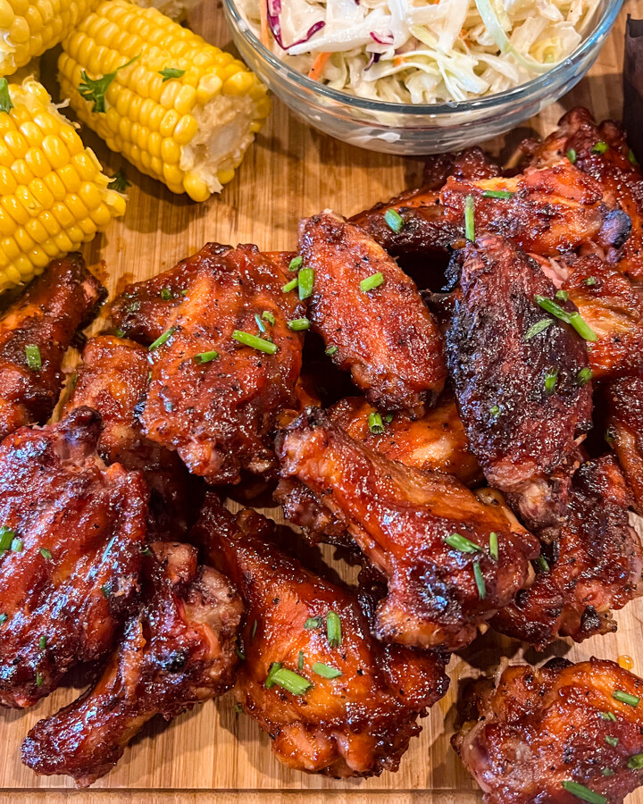 Glazed smoked chicken wings on a platter with corn and other sides.