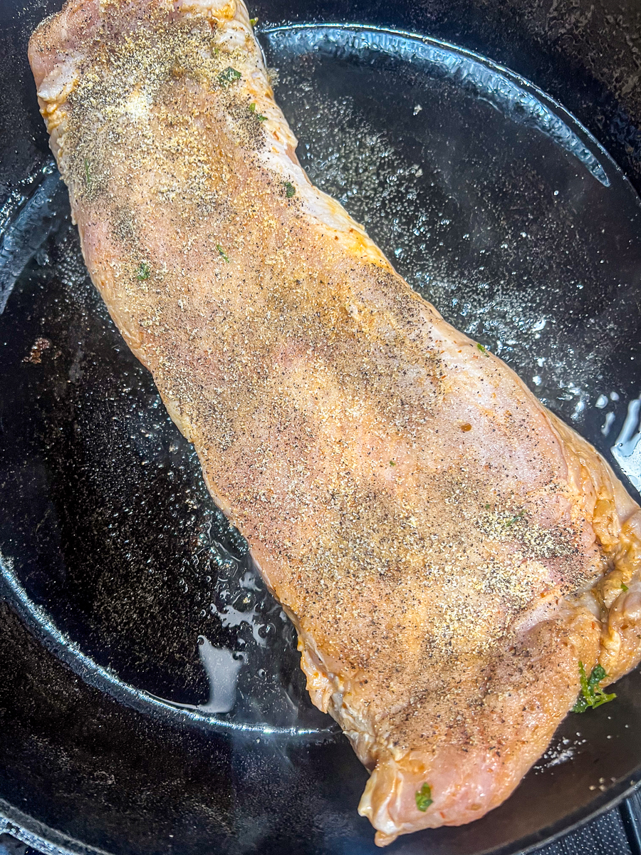 Seasoned pork tenderloin being seared in a cast iron skillet.