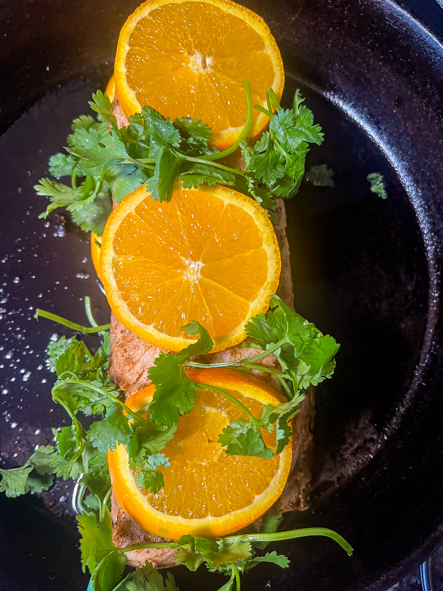 The pork nestled between layers of orange slices and cilantro for baking.