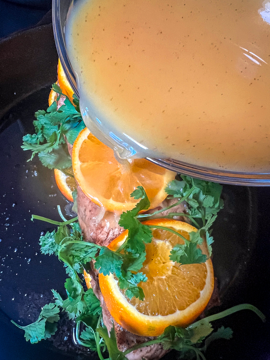Seasoned orange juice being poured over the pork in the skillet.