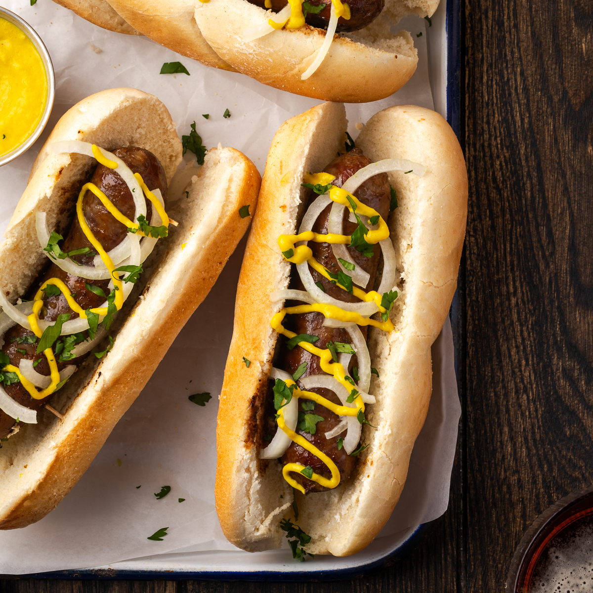Braised beer brats on buns topped with toppings to serve as a sandwich.