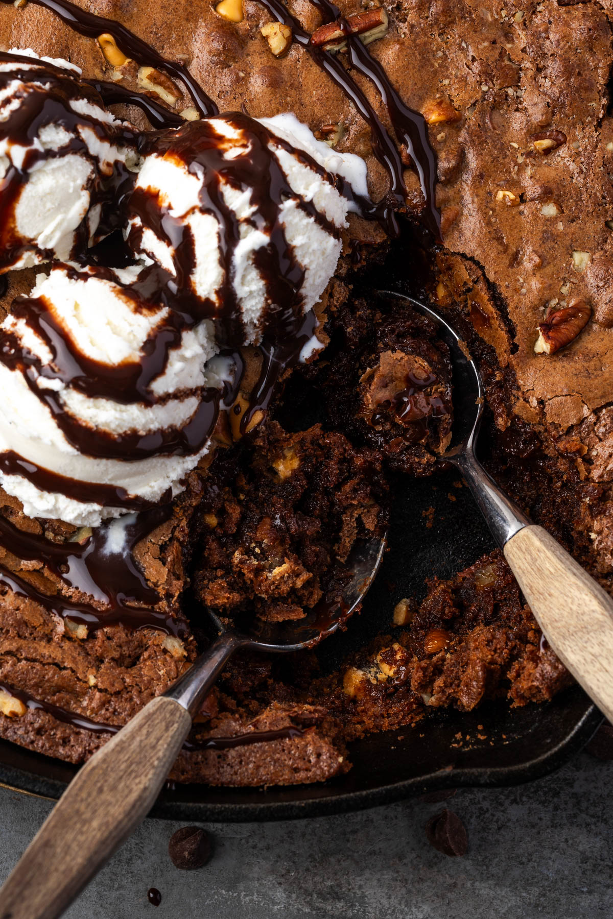 Butterscotch brownies in a skillet topped with ice cream and spoonfuls missing.