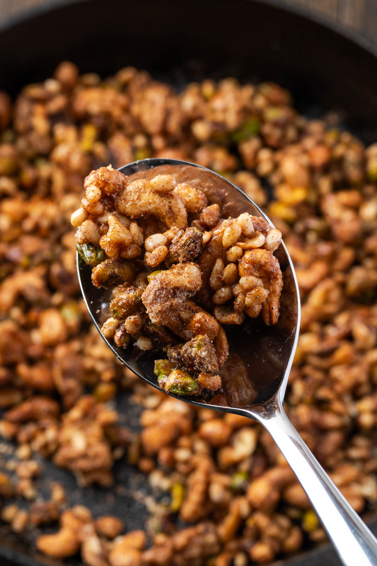 A spoonful of cinnamon nuts held up over a skilelt of more.