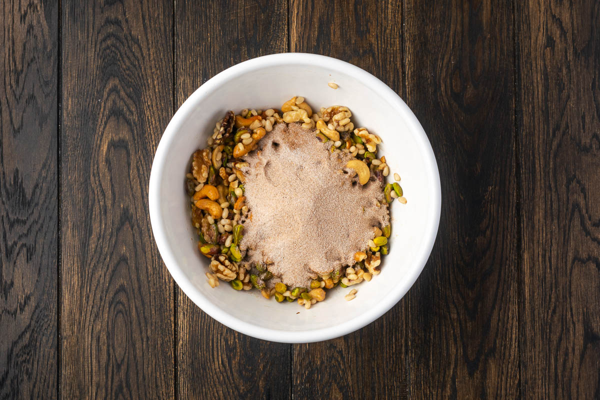 Sugar and spice mixture added to the bowl of nuts.
