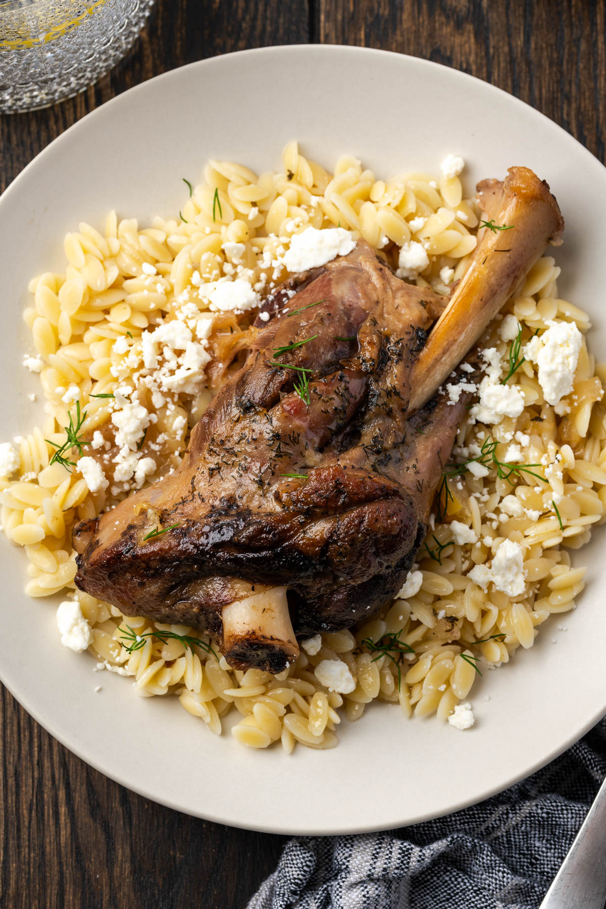 Lamb shanks served over a plate of orzo with feta cheese sprinkled over the top.