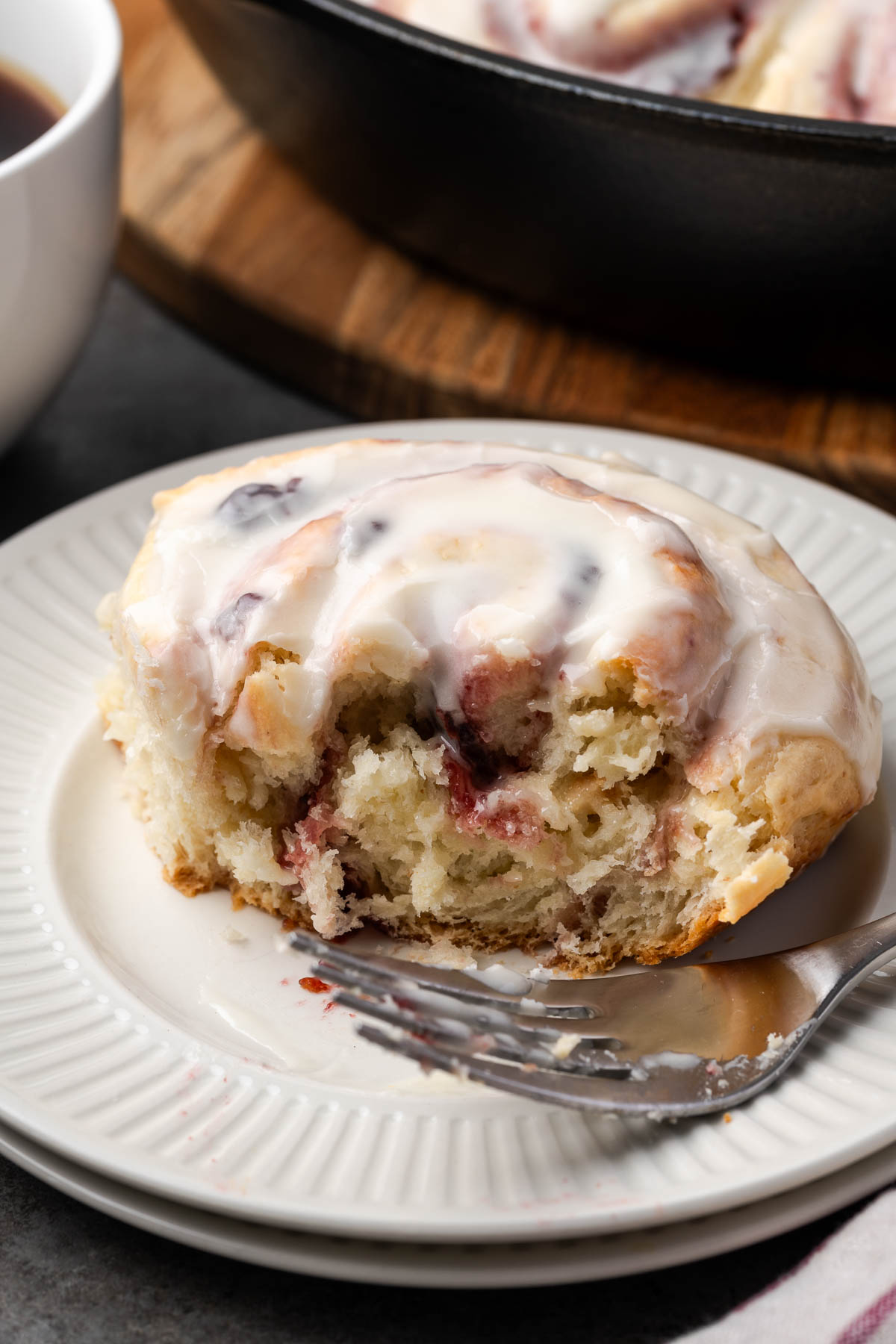 A cherry sweet roll with a bite cut to show inside and a fork to the side.