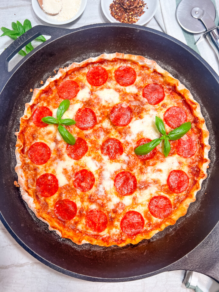 A cast iron pizza garnished with fresh basil.