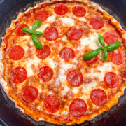 A cast iron pizza with pepperoni, garnished with basil.