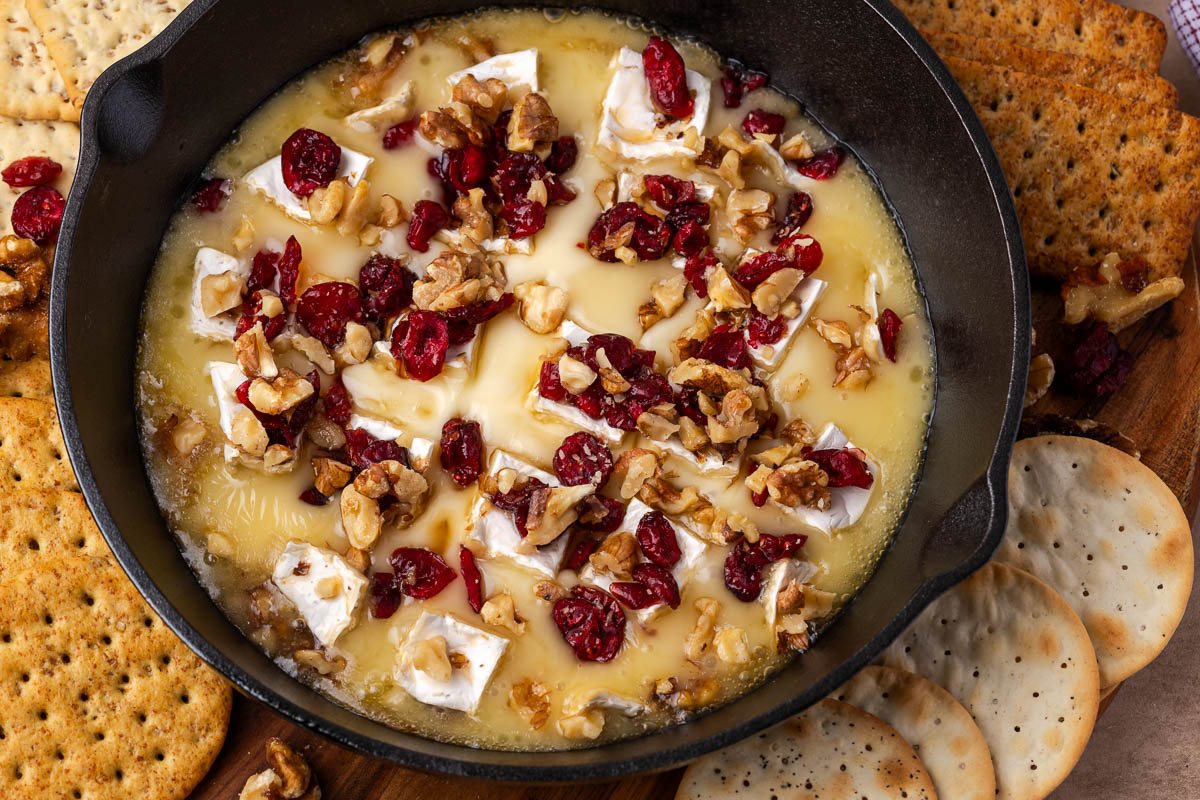 Baked cranberry brie in a skillet with crackers all around it.