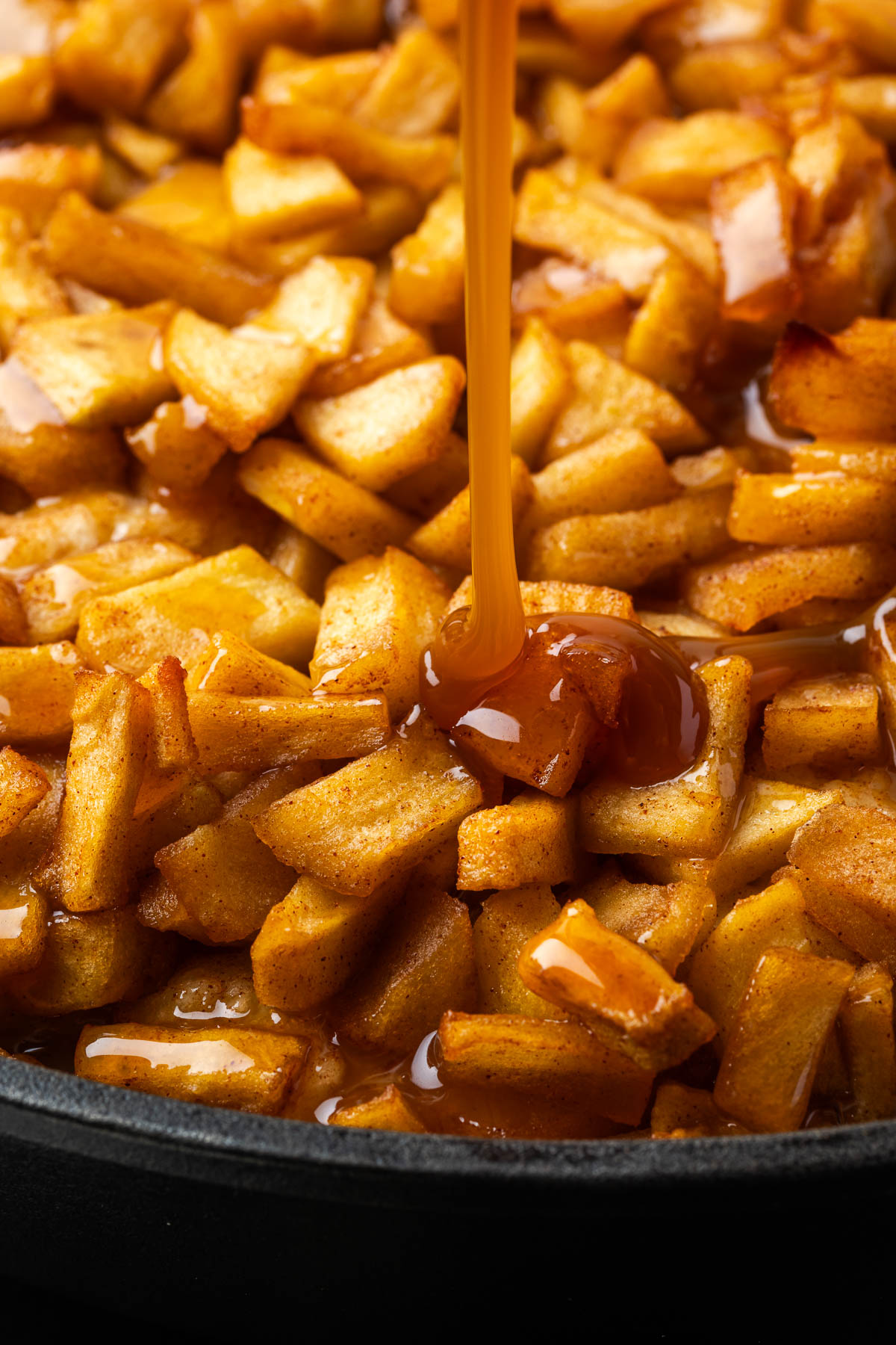 Pouring caramel sauce on top of the apples and pizza dough.