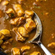 A spoon lifting a serving of easy chicken curry from a skillet.