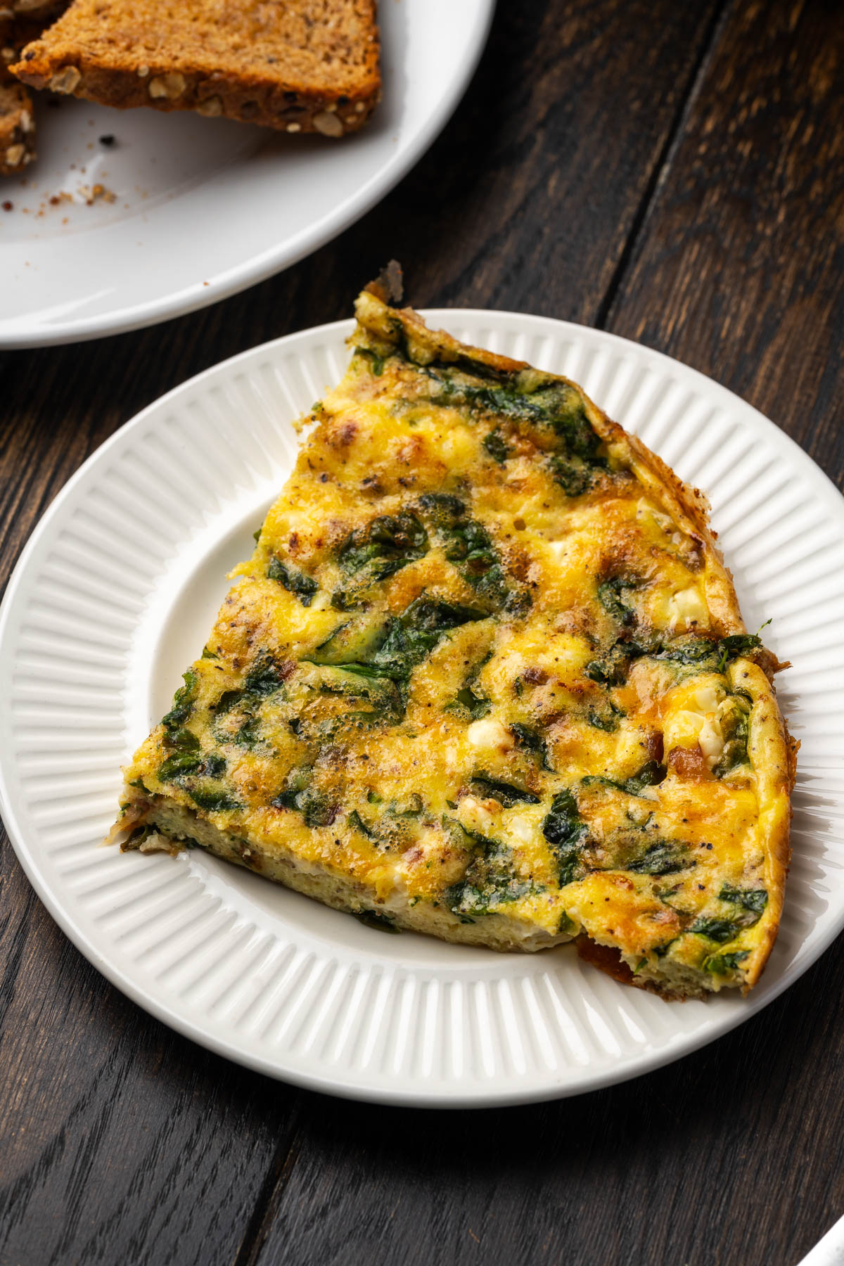 A slice of spinach frittata on a white plate. 