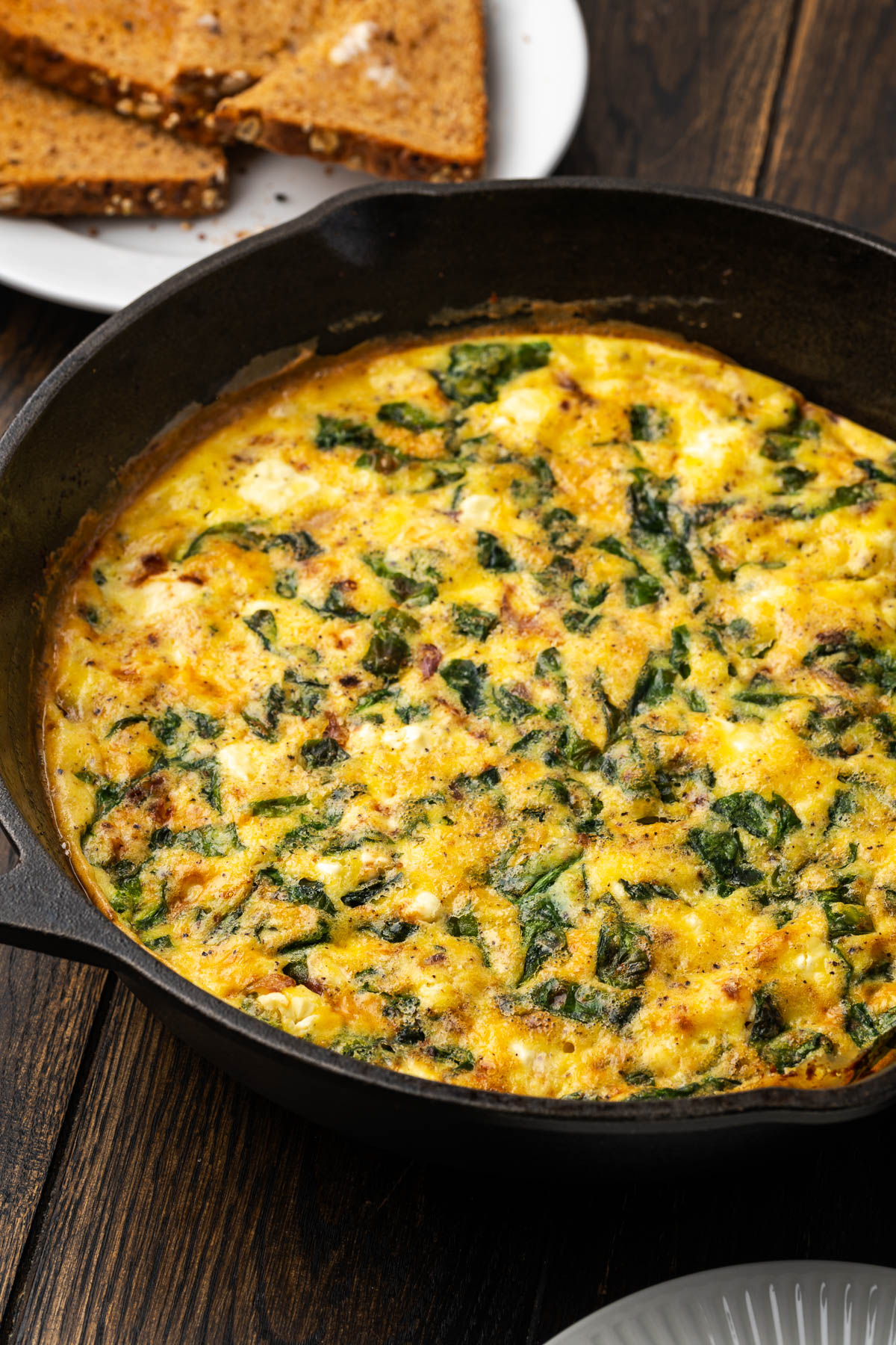Spinach frittata cooked in a cast iron skillet on the table with a plate of toast.