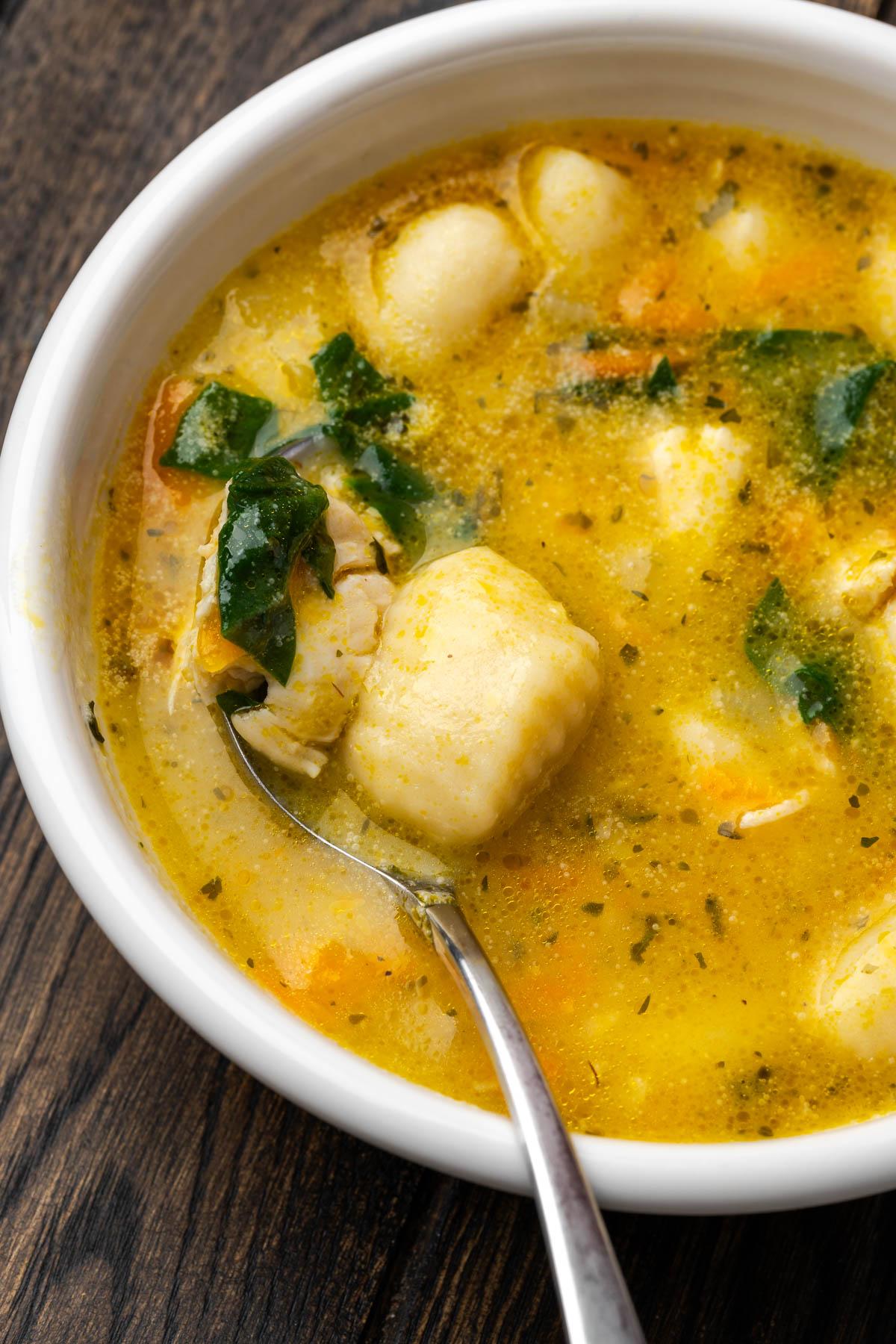 A bowl of creamy chicken gnocchi soup with a spoon in the bowl lifting up a bite. 