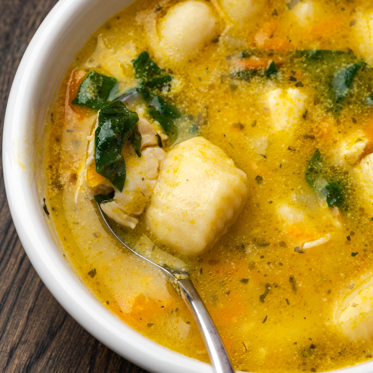 A bowl of creamy chicken gnocchi soup with a spoon in the bowl.