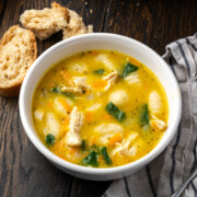 A bowl of creamy chicken gnocchi soup on a table with bread to the side.
