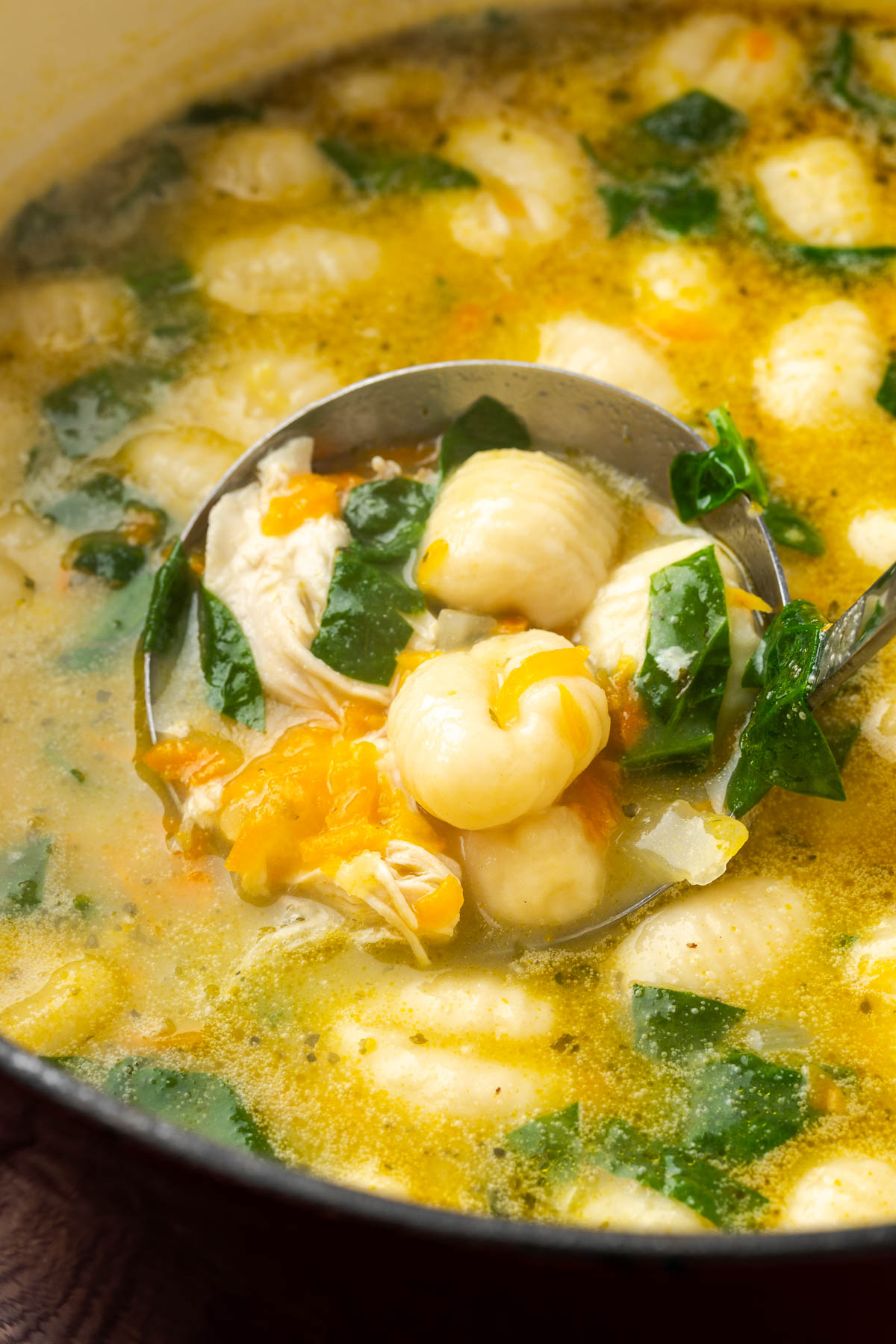 A ladle scooping up a spoonful of creamy chicken gnocchi soup from the pot.