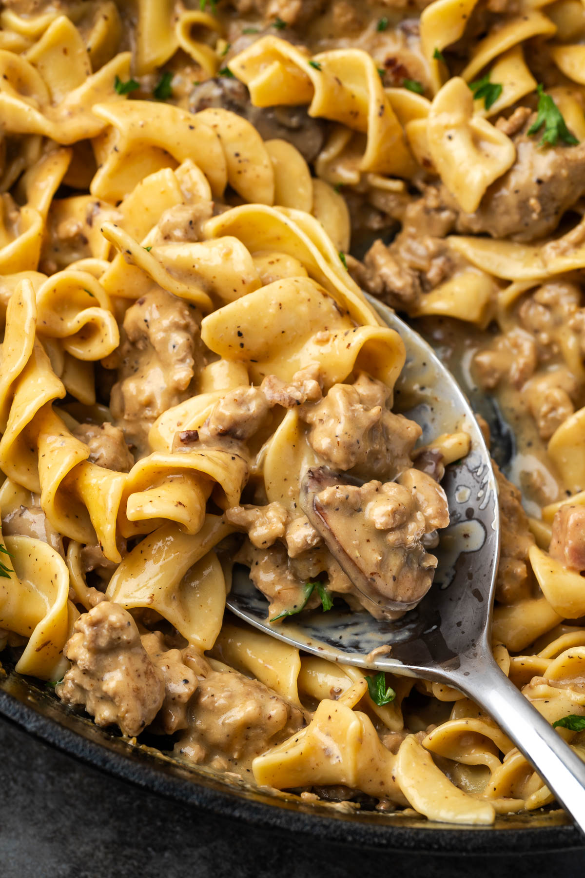 A skillet of ground turkey stroganoff with a spoon lifting up a serving.