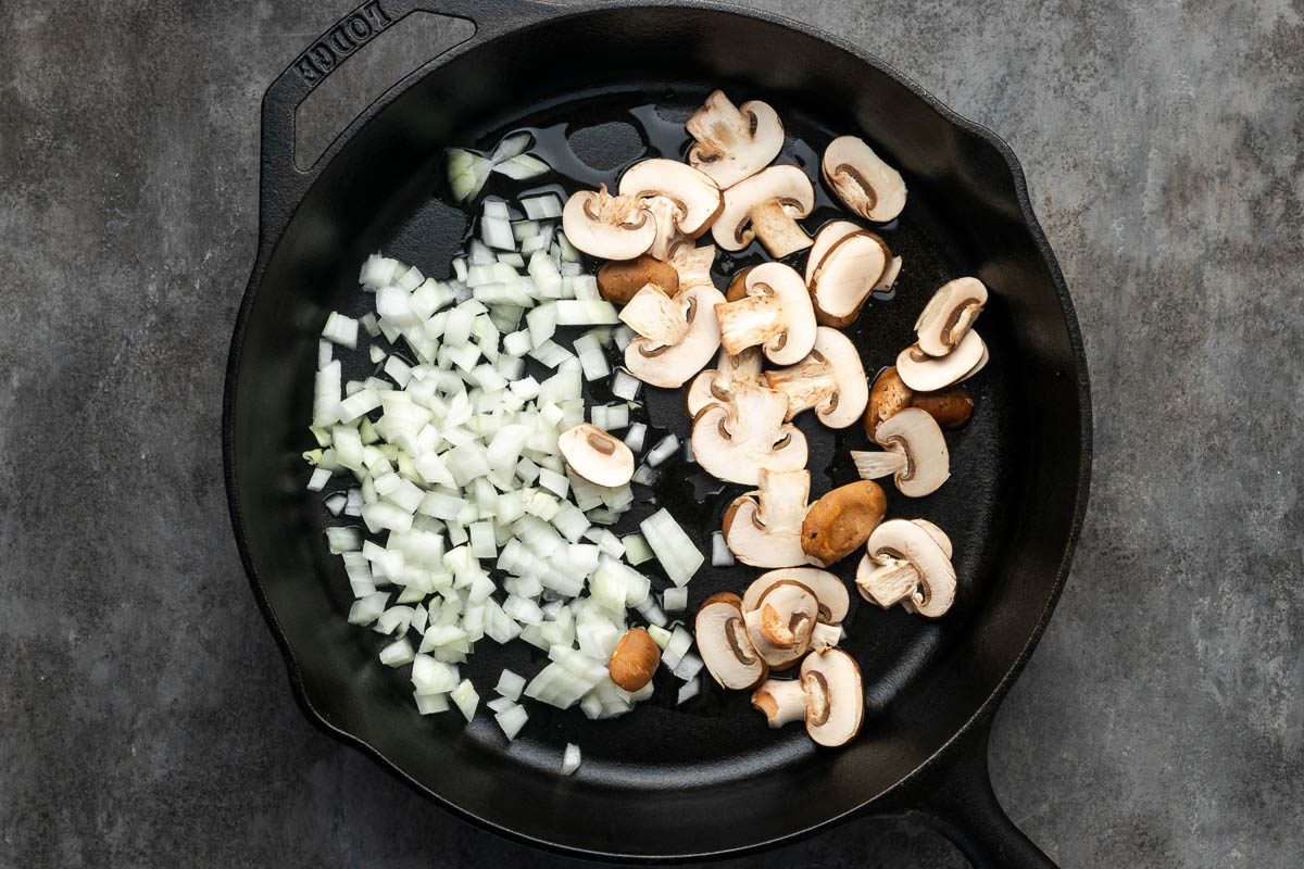 Onions and mushrooms added to a skillet to cook.