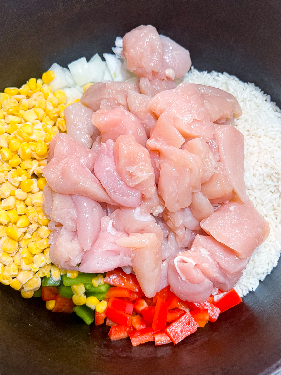 Instant rice, frozen corn, bell peppers, onions, and diced chicken in a dutch oven.