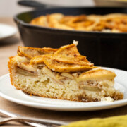 A slice of skillet cake on a plate with the skillet in the background.