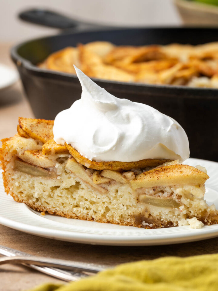 A slice of skillet cake with apples on a plate topped with whipped cream.