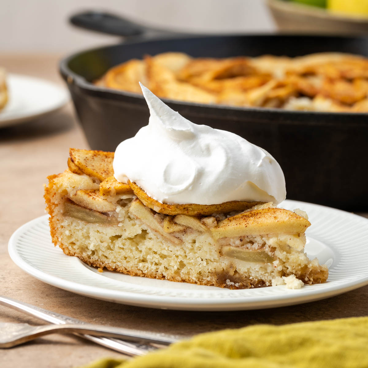 A slice of skillet cake with apples on a plate topped with whipped cream.