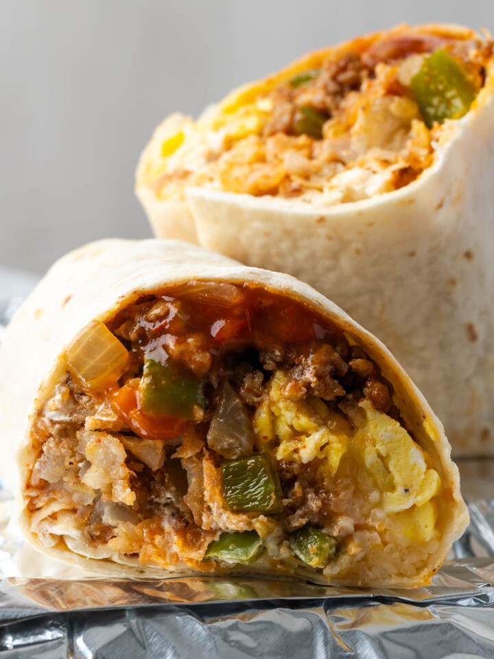 A homemade sausage breakfast burrito cut in half on a piece of foil.