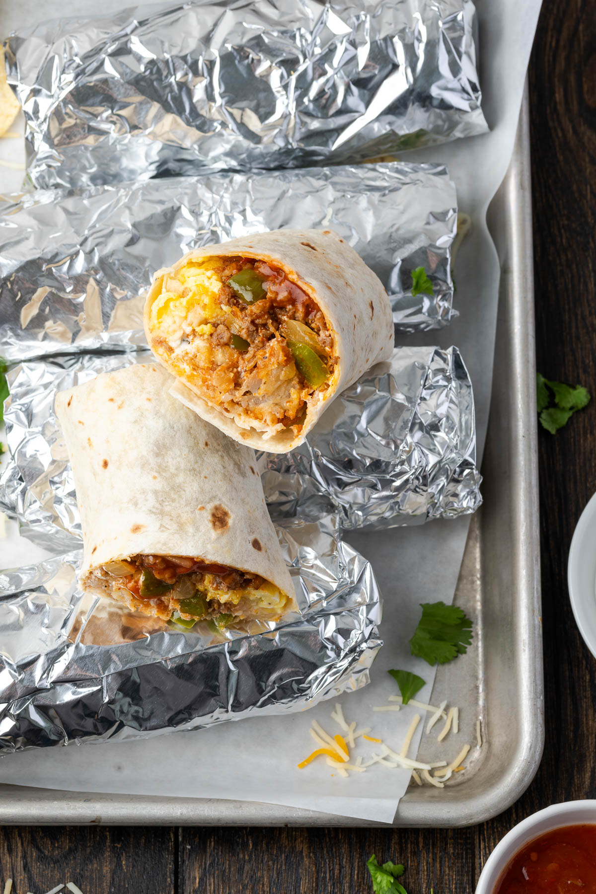 Wrapped homemade breakfast burritos on a pan with one open and cut in half on the edge.