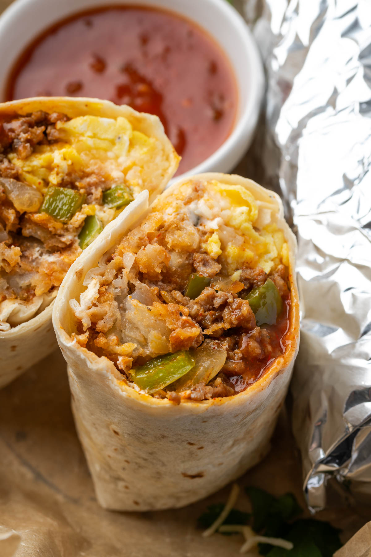 Sausage breakfast burritos cut in half with a bowl of salsa to the side.