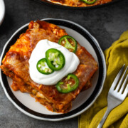 A serving of enchilada skillet on a plate with sour cream and jalapenos on top.