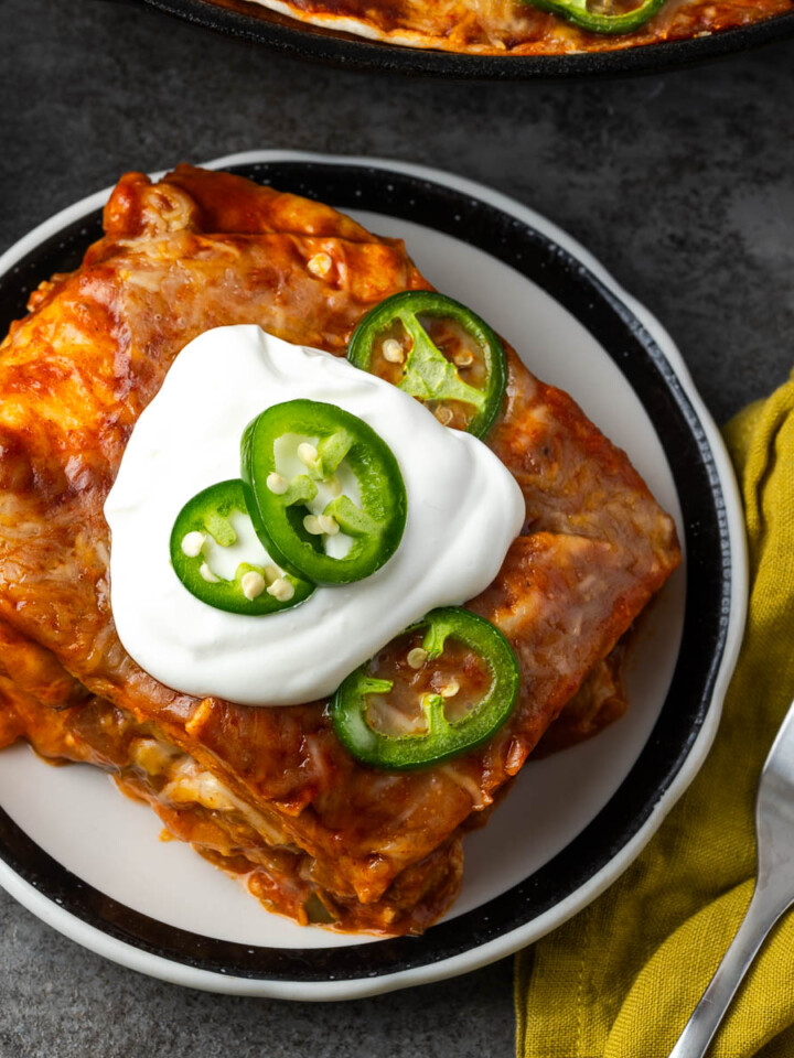 A serving of enchilada skillet on a plate with sour cream and jalapenos on top.