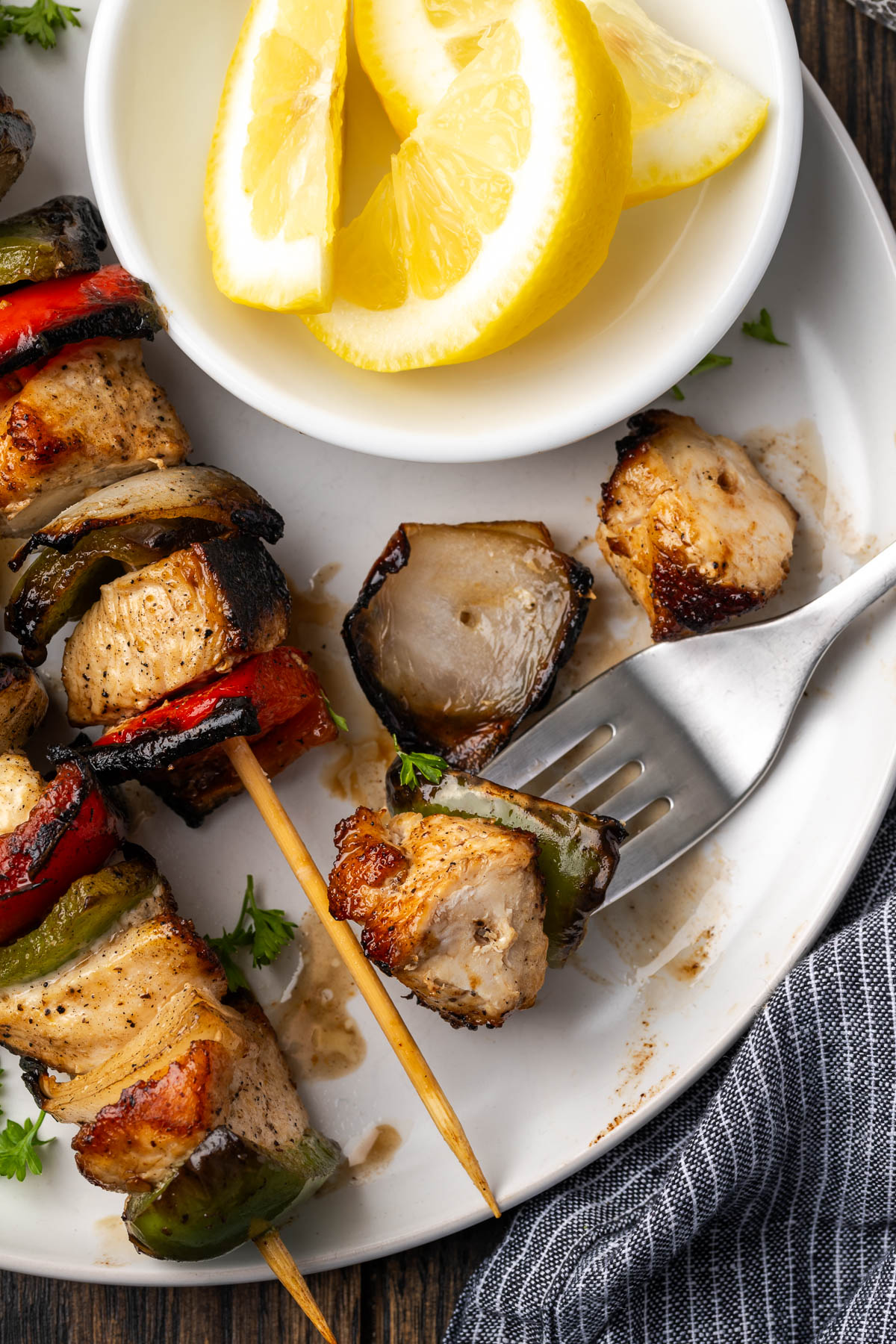 Chicken and vegetable kabobs on a white plate next to a bowl of lemons.