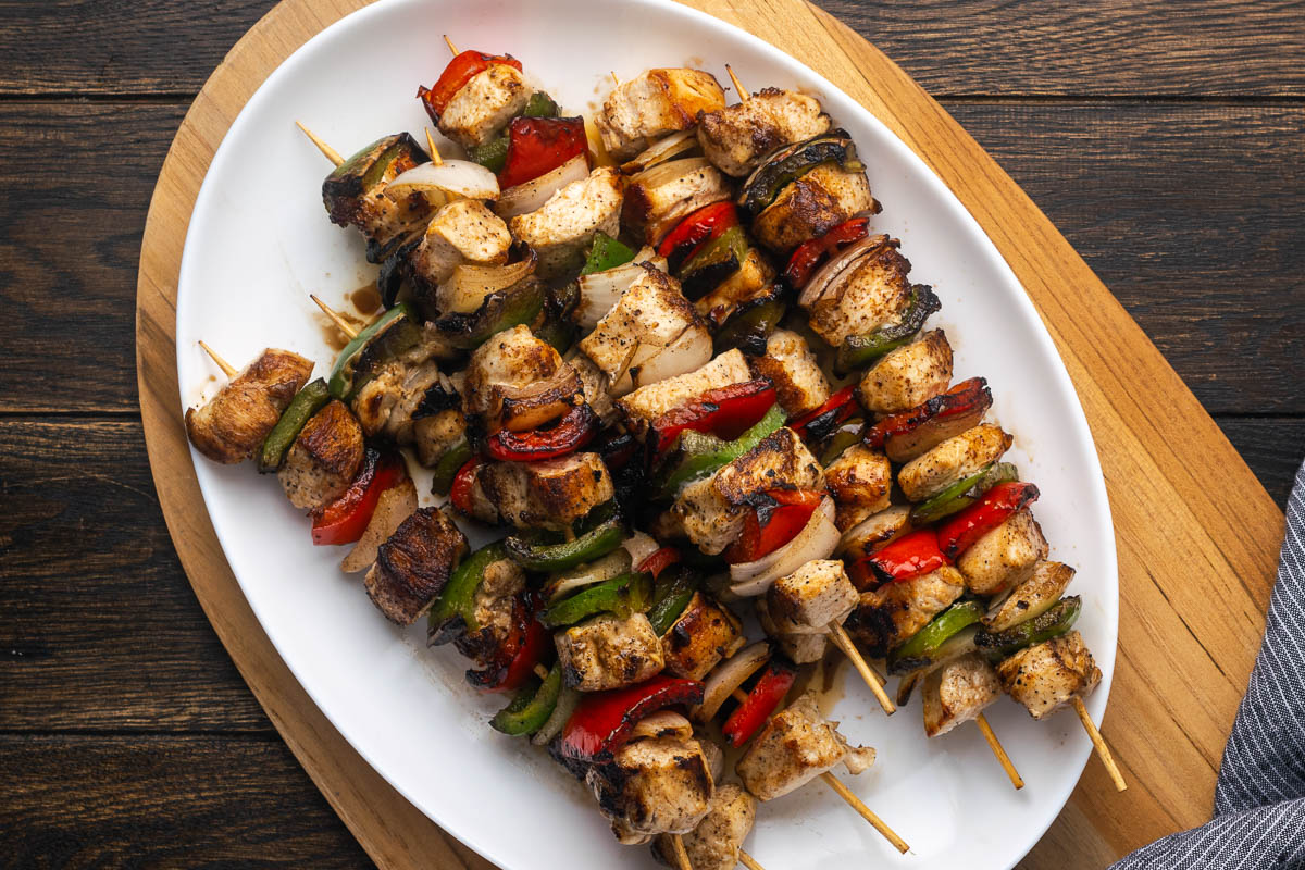 A pile of chicken kabobs on an oval white platter.