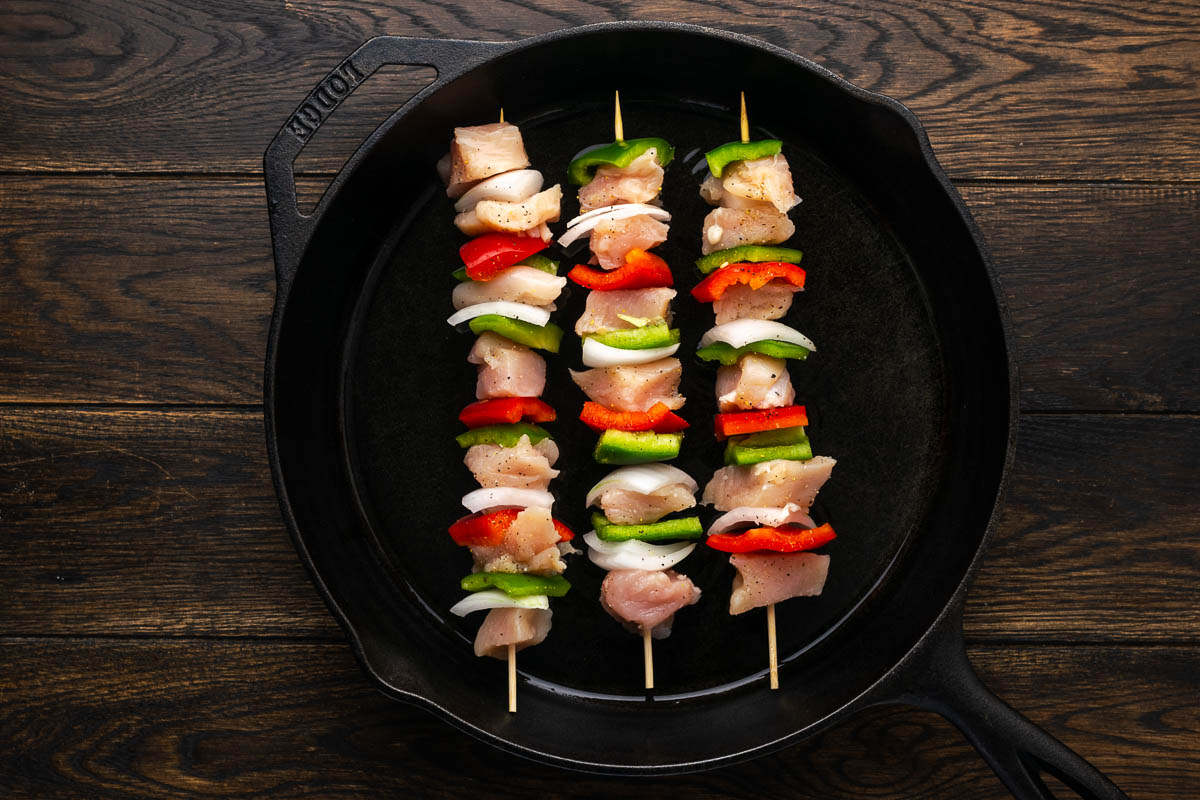 Chicken kabobs cooking in a skillet on the stove.