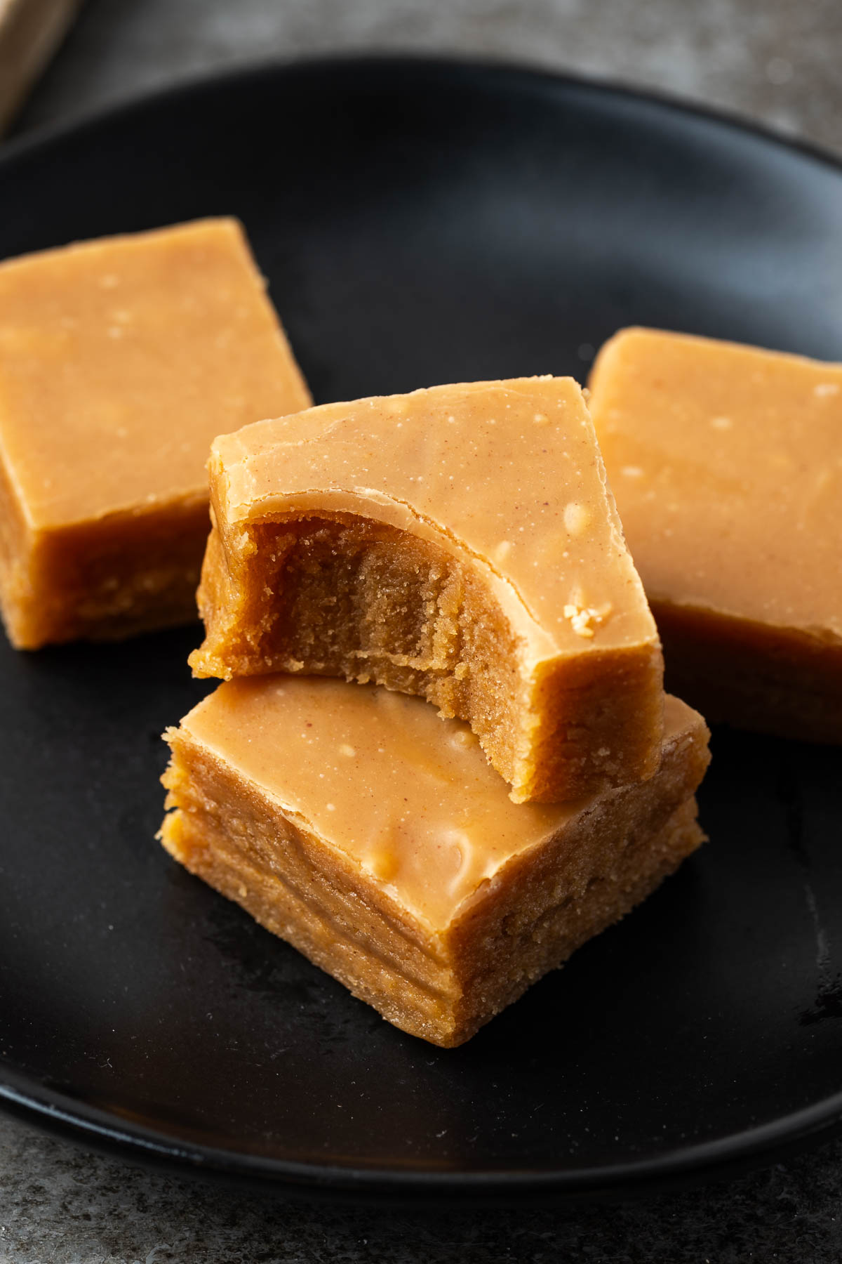 Peanut butter fudge on a surface with two pieces stacked and a bite missing from the one on top.
