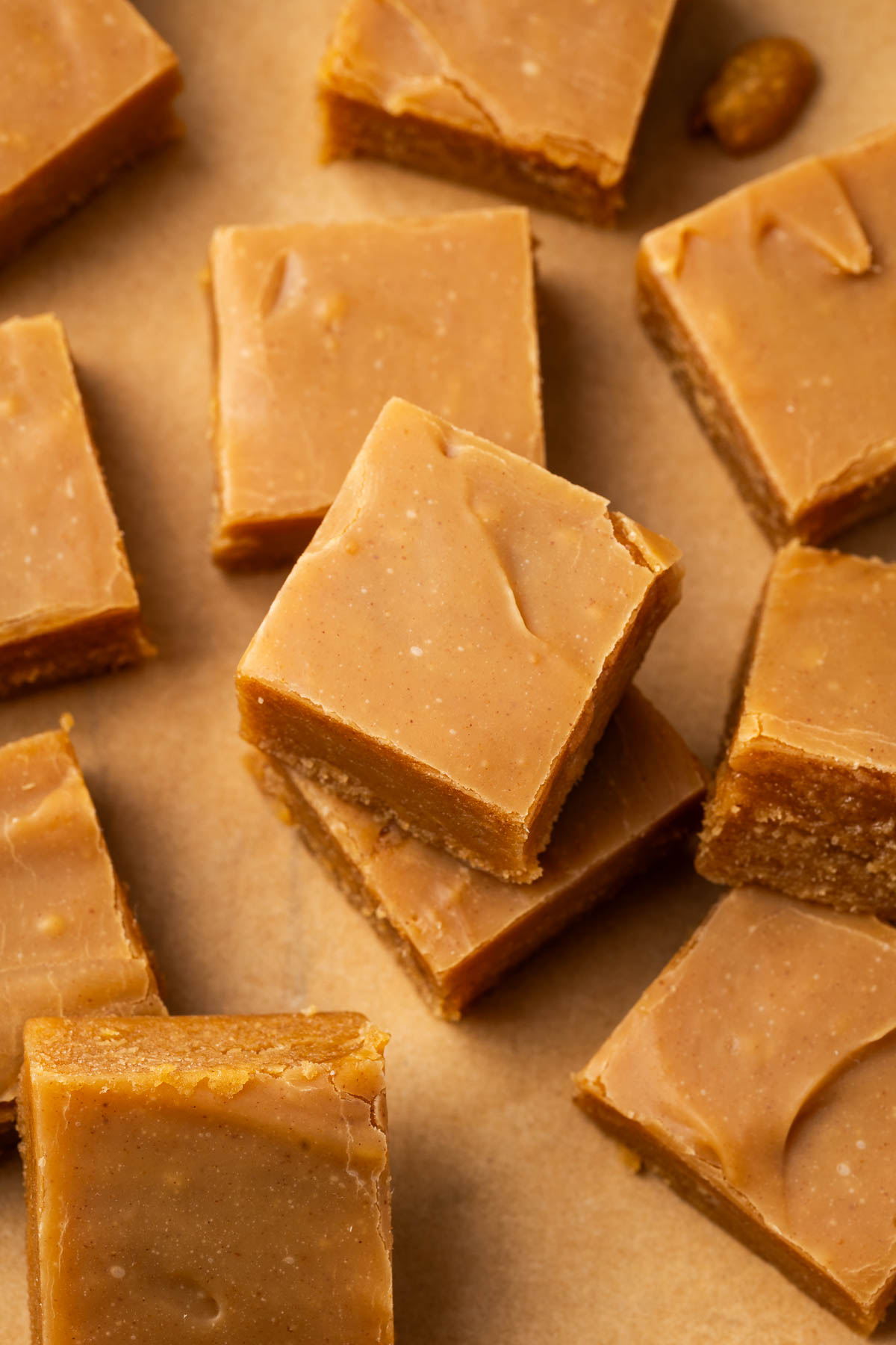 Squares of peanut butter fudge laid out in different angles and some stacked on parchment paper.