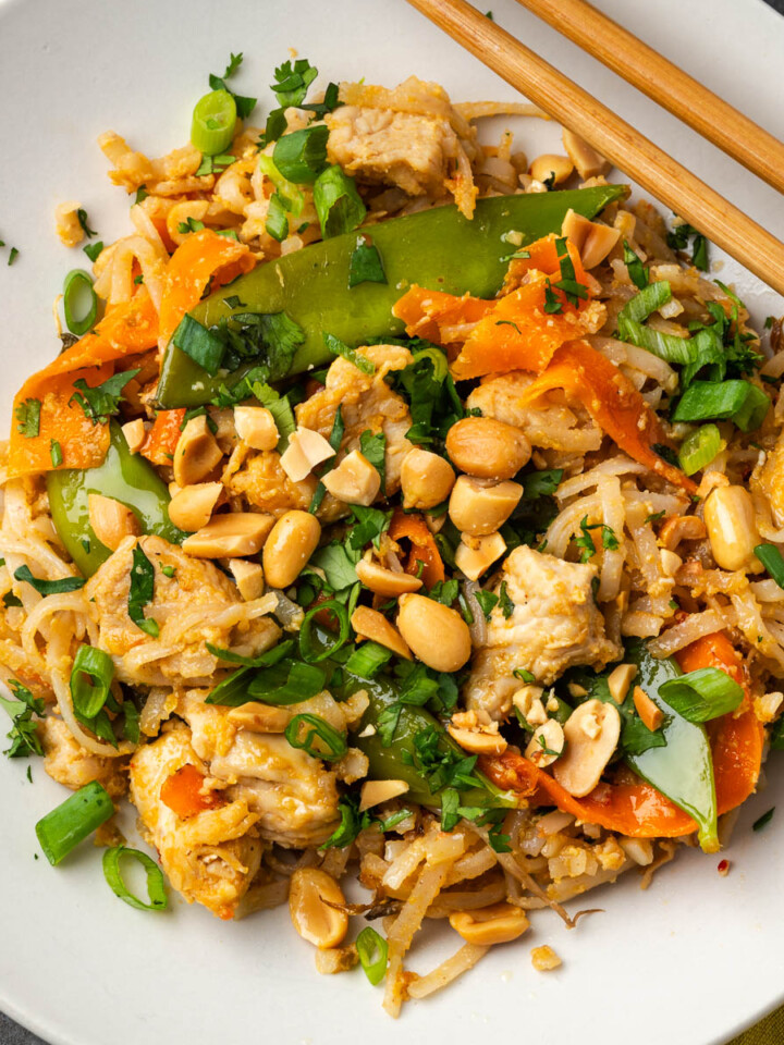 Peanut chicken stir fry with noodles in a bowl and chopsticks resting on the edge of the bowl.