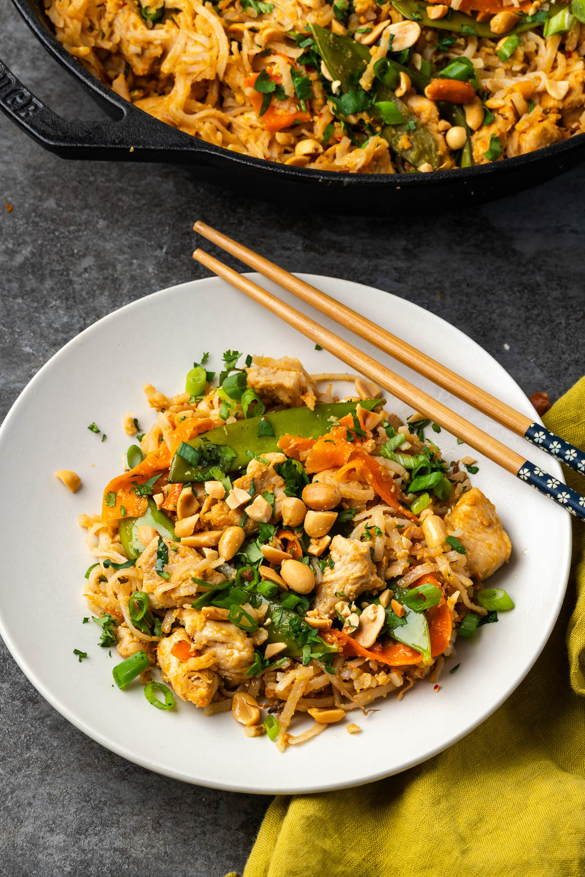 Peanut chicken stir fry in a white bowl with the skillet of more in the background.