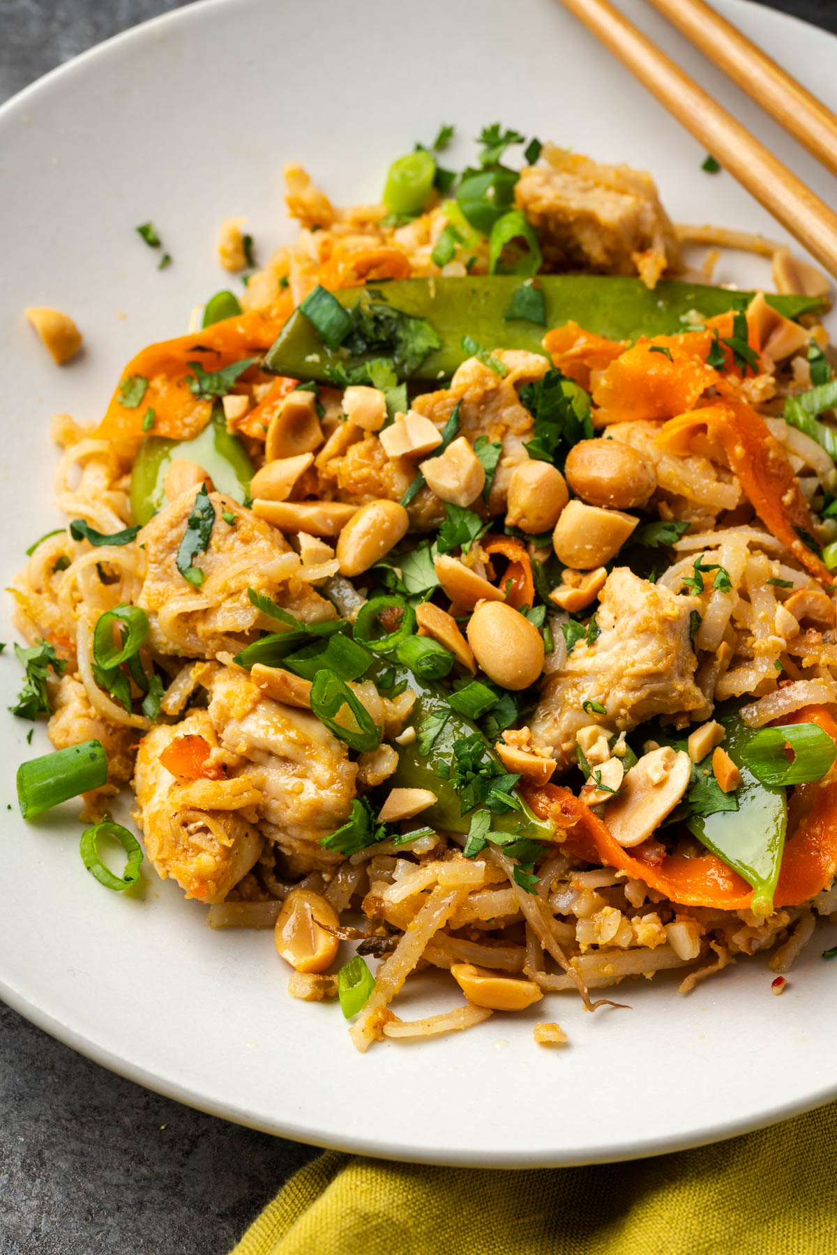 Peanut chicken stir fry with noodles in a bowl with chopsticks resting on the edge of the bowl.