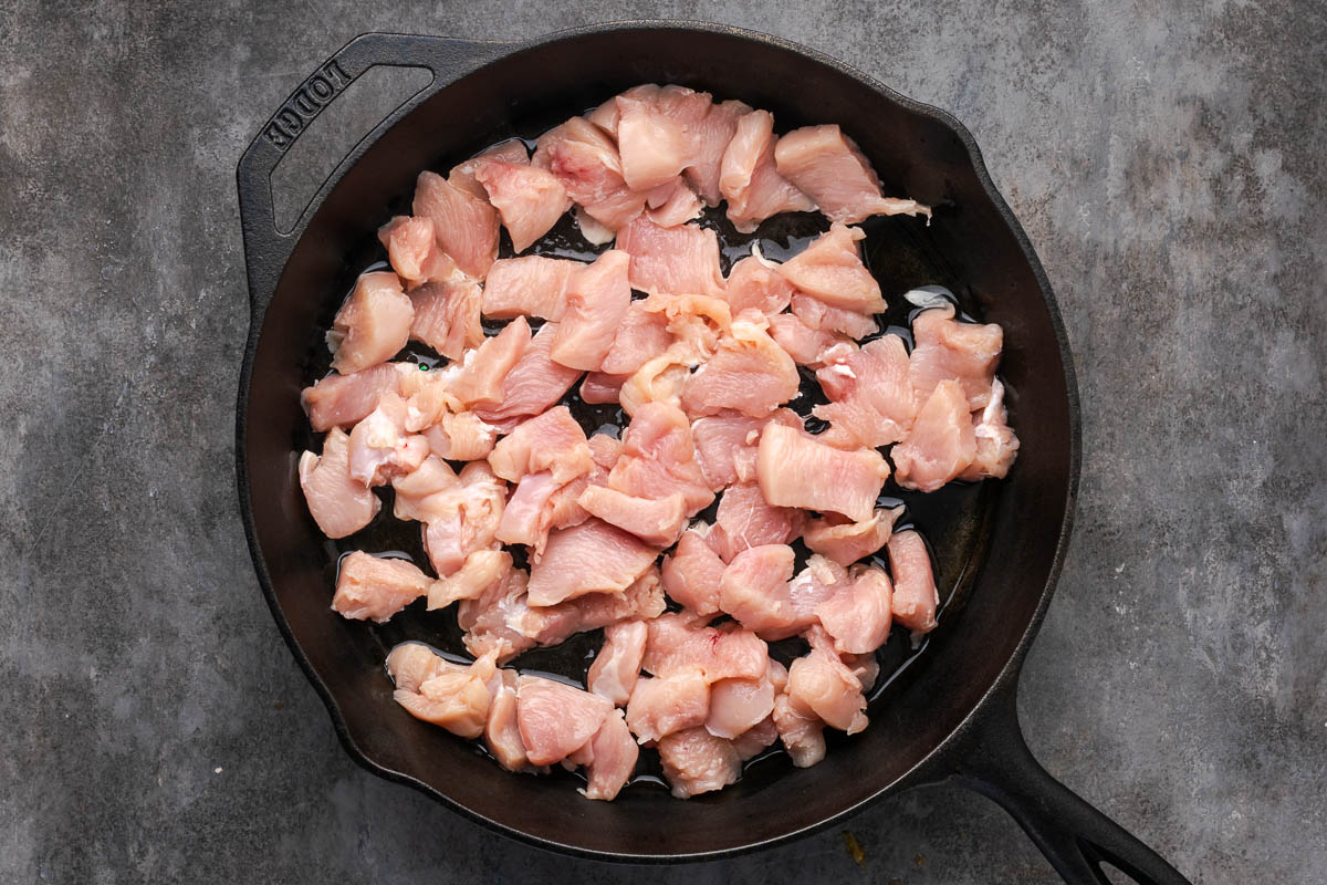Diced chicken added to a cast iron skillet.