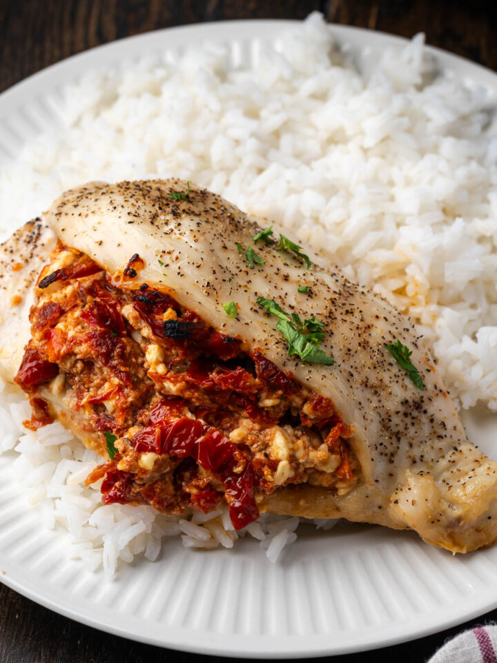 Sun dried tomato stuffed chicken breast on a plate with rice.