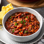 A bowl chuck wagon brisket and beans with pieces of cornbread on the edge of the plate.