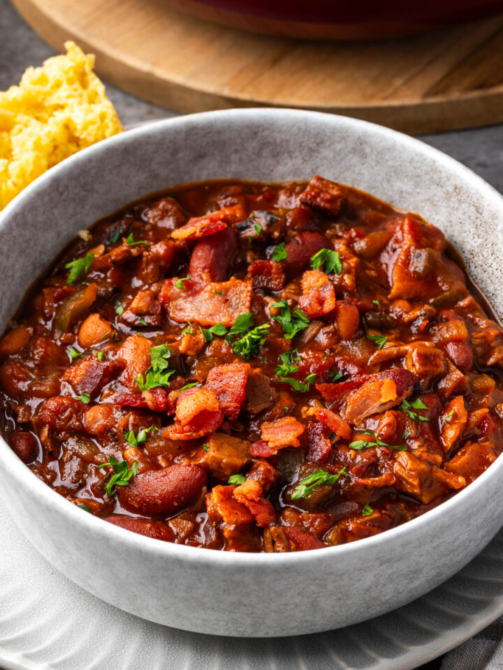 A bowl chuck wagon brisket and beans with pieces of cornbread on the edge of the plate.