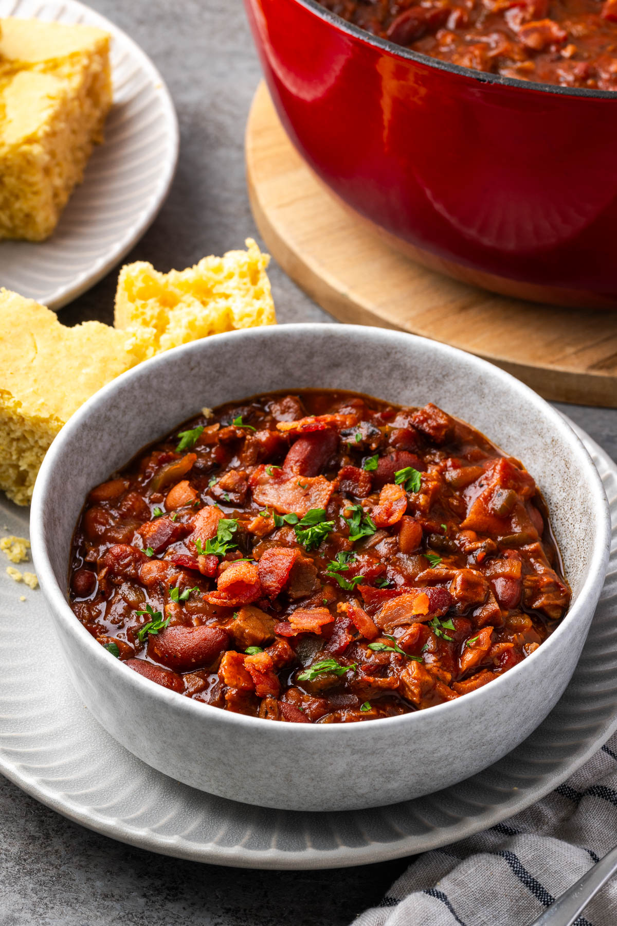 A bowl of brisket and beans on a plate with the pot in the back. 