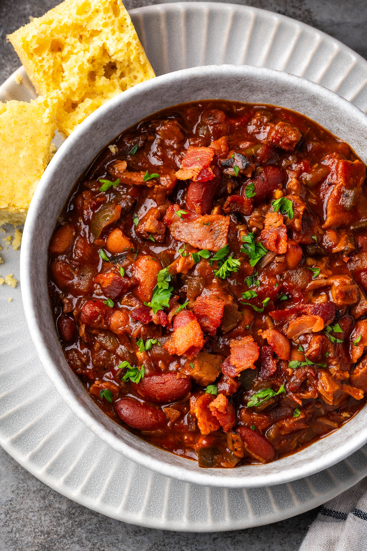 A bowl of brisket and beans on a plate with cornbread to the side.