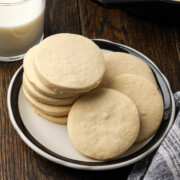 Skillet sugar cookies stacked on a plate and some leaning over.