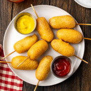 Homemade mini corn dogs on a white plate with a napkin to the side.