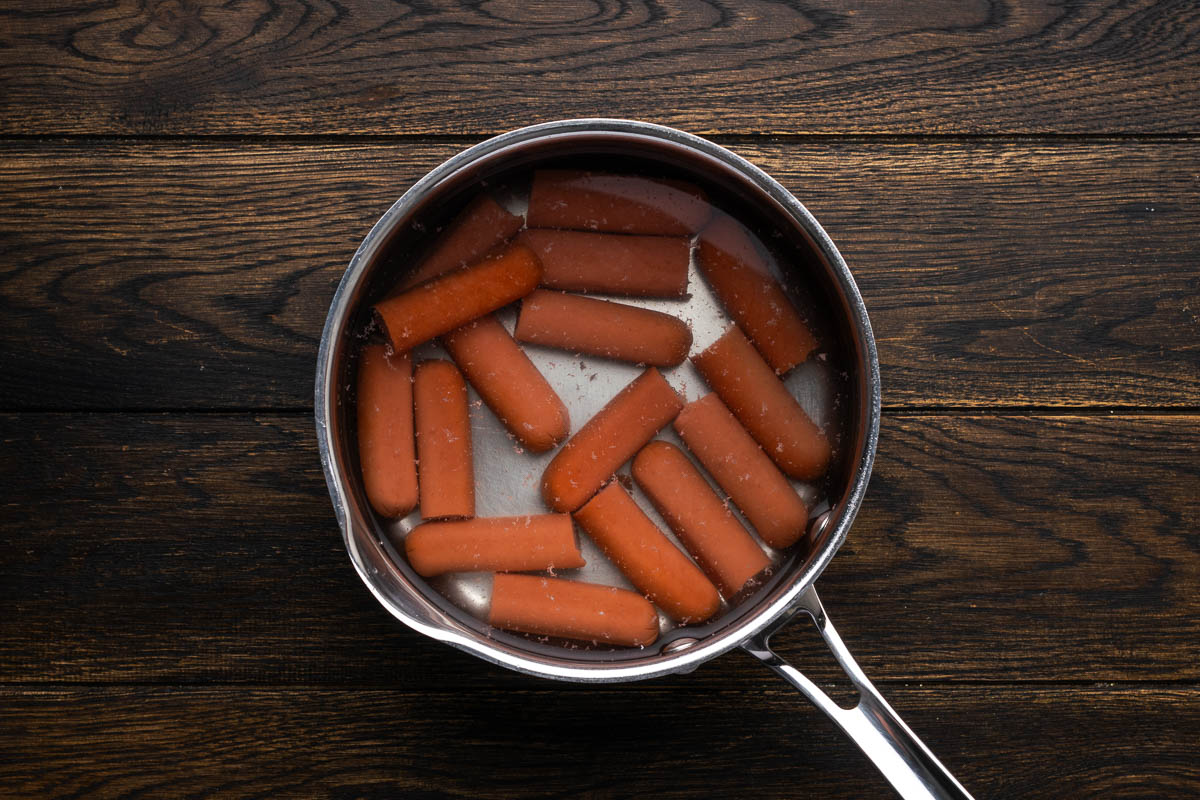 Hot dogs cooking in a saucepan.