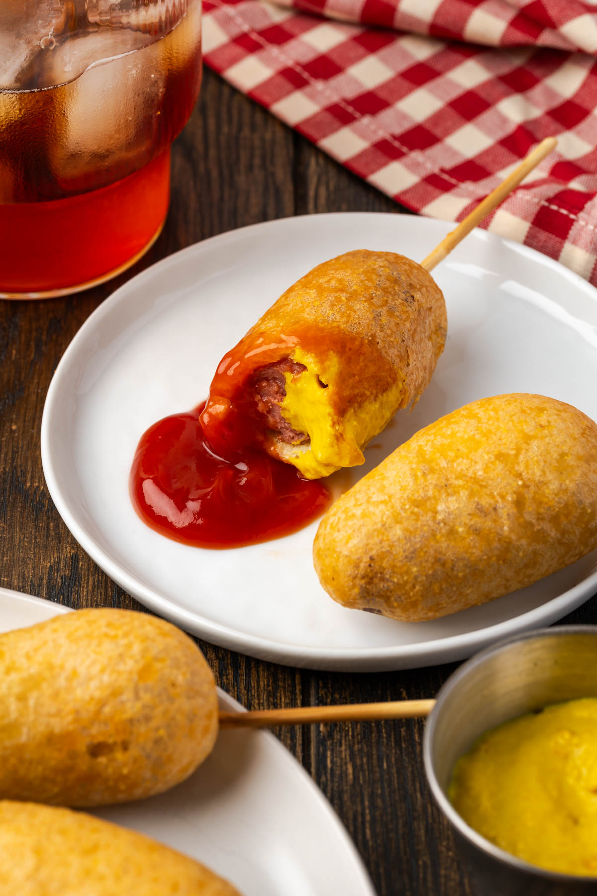 Homemade corn dogs on a plate with ketchup and a bite missing from one.